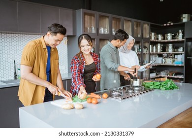 Friend Cooking Together In The Kitchen While Looking At Online Course From Tablet Pc