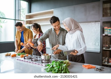 Friend Cooking Together In The Kitchen While Looking At Online Course From Tablet Pc