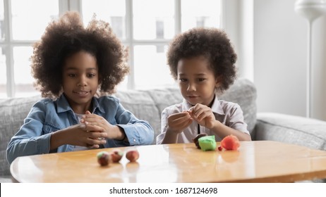 Friendly African little sister and small brother spend time together seated on couch holding playdough sculpt with plasticine create different shapes. Activity at home, pastime craft and hobby concept - Powered by Shutterstock