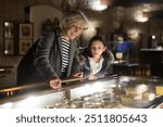 Friendly aged female tutor helping preteen girl exploring antique showpieces in local history museum..