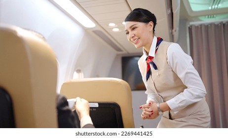Friendly Asian female flight attendant serving food drink and talking to passengers on airplane. Airline service