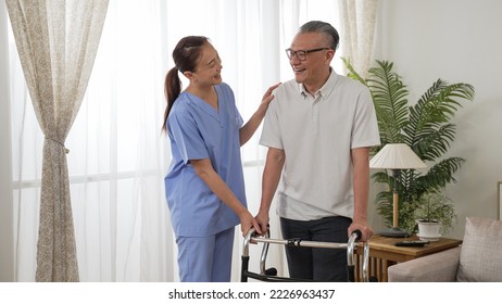 Friendly Asian Personal Care Attendant Chatting With Mature Male Patient While He Is Standing With A Walker Near The Window At Home