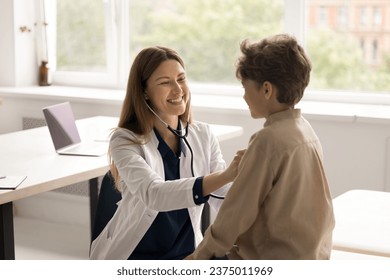 Friendly attractive woman pediatrician in medical coat hold stethoscope listen heartbeat of little boy. Smiling young specialist checks breath of small cute patient. Health check, pediatry, healthcare - Powered by Shutterstock