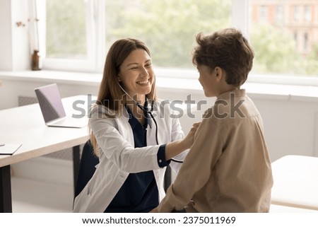 Friendly attractive woman pediatrician in medical coat hold stethoscope listen heartbeat of little boy. Smiling young specialist checks breath of small cute patient. Health check, pediatry, healthcare