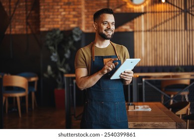 Friendly barista in an apron smiles while using a digital tablet inside a contemporary coffee shop. The atmosphere is warm and inviting, showcasing the blend of technology and personal service. - Powered by Shutterstock