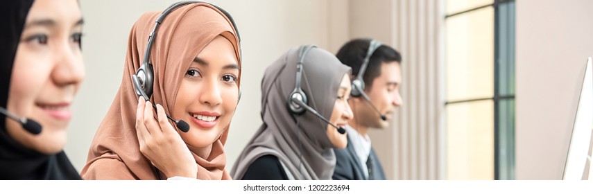 Friendly Beautiful Asian Muslim Woman Wearing Microphone Headset Working As Customer Care Operator With Team In Call Center Office, Panoramic Web Banner