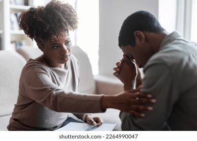 Friendly beautiful black woman therapist consoling upset young man, african american female psychologist touching sad crying patient shoulder, clinic interior. Psychological support concept - Powered by Shutterstock