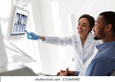 Friendly Black Female Dentist Showing Patient His Teeth On Xray, Using Digital Display, Copy Space