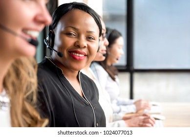 Friendly Black Woman Wearing Microphone Headset Working In Call Center With International Team As Telemarketing Customer Service Agents