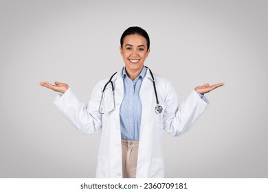 Friendly brazilian female doctor in uniform showing both hands open palms, leaving choice to patient, presenting and advertising comparison and balance over grey background - Powered by Shutterstock