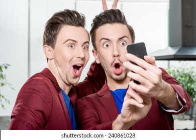 Friendly brothers twins having fun taking selfie photo with smart phone in the white home or restaurant interior