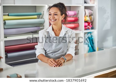 Friendly brunette woman leaning on a counter in front of shelves with fancy paper rolls