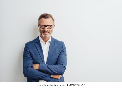 Empresário amigável usando óculos e um terno posando com os braços cruzados sorrindo para a câmera contra um fundo branco de estúdio com espaço de cópia