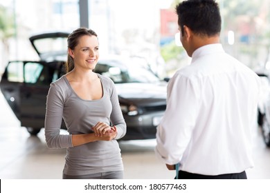 Friendly Car Salesman Talking To A Young Woman Inside Showroom