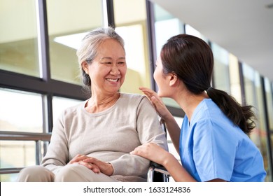 Friendly Caregiver Of Nursing Home Talking To Asian Senior Woman In Hallway