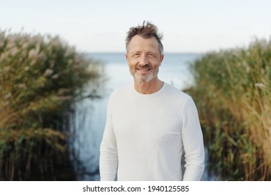 Friendly cheerful bearded middle-aged man at the seaside standing smiling at the camera against a backdrop of the sea and reed beds on a cold overcast day - Powered by Shutterstock