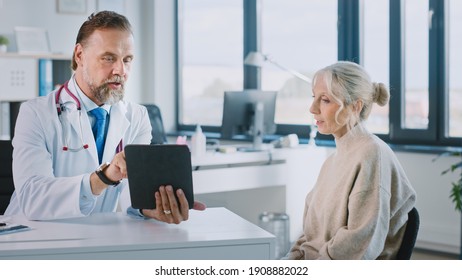 Friendly and Cheerful Family Doctor is Reading Medical History of Senior Female Patient During Consultation in a Health Clinic. Physician Using Tablet Computer in Hospital Office.