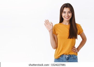Friendly cheerful, happy smiling woman waving you with raised hand. Attractive girl greeting friend, say hello or hi, welcome guest, standing white background joyful, express positivity and joy