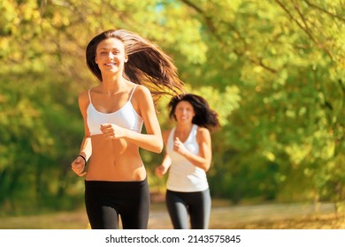 Friendly Compteition. Shot Of Two Young Women Jogging Together In A Park In Autumn.