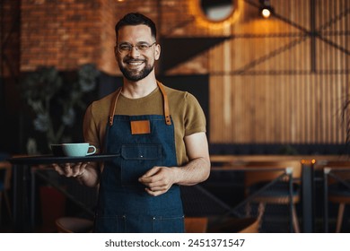 Friendly confident male owner at his cafe. Portrait of happy waiter in a cafe looking at camera. Copy space. Profesional Waiter in Restaurant  - Powered by Shutterstock