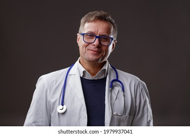 Friendly Confident Middle-aged Male Doctor In Lab Coat And Stethoscope Looking At The Camera With A Charismatic Genuine Smile Over A Dark Studio Background