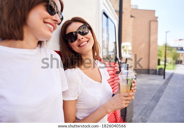 Friendly conversation. Pretty\
girl keeping smile on her face while looking at her sister at the\
street