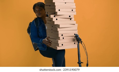 Friendly courier clutching many packages in her hands for a party event in urban area. Black woman carefully balances large order for food delivery ensuring customer satisfaction - Powered by Shutterstock