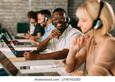 Friendly customer support agent smiling while working with colleagues using headsets in a modern office environmen