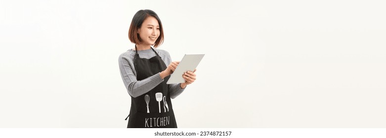 Friendly cute female barista in black apron smiling at camera, using digital tablet to manage cafe orders - Powered by Shutterstock