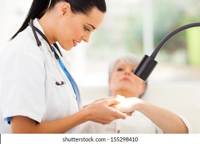 friendly dermatologist examining senior woman's skin under light - Powered by Shutterstock