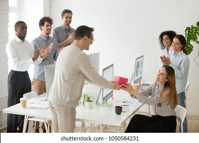 Friendly Diverse Corporate Team Congratulating Happy Female Colleague With Birthday And Applauding, Male Employee Presenting Gift Box Greeting Woman Making Pleasant Surprise To Coworker In Office