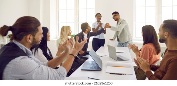 Friendly And Diverse Employees Congratulate Man On Business Achievements, Excellent Work Results Or Promotion. Business People Applaud And Cheers During Business Meeting In Bright Modern Office.