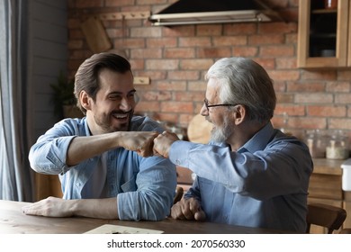Friendly draw. Happy joyful two men of different age give fist bump after ending game of checkers draughts. Laughing elderly father retiree and millennial son greet each other with finishing boardgame