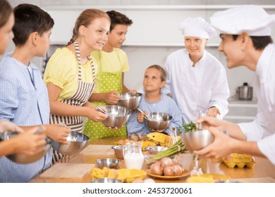 Friendly enthusiastic tween girl learning how to cook and listening to advices of professional chef during group cooking masterclass .. - Powered by Shutterstock