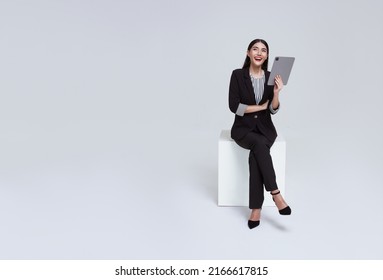friendly face asian businesswoman smile in formal suit sitting on chair her using tablet and looking to copyspace isolated on white background studio shot.