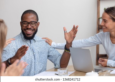 Friendly Female Caucasian Team Employees Tap African American Male Colleague On The Shoulder Supporting Cheering Mate Congratulating Happy Black Coworker With Promotion Reward, Recognition Concept