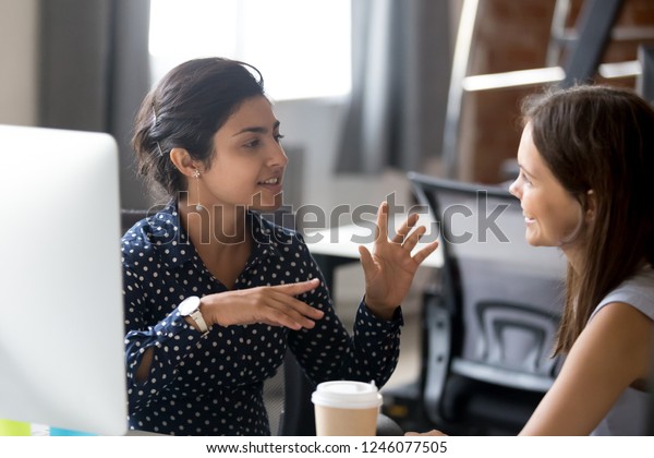Friendly female colleagues having good\
relationships, pleasant conversation at workplace during coffee\
break, smiling young woman listen talkative coworker, discussing\
new project, talking in\
office