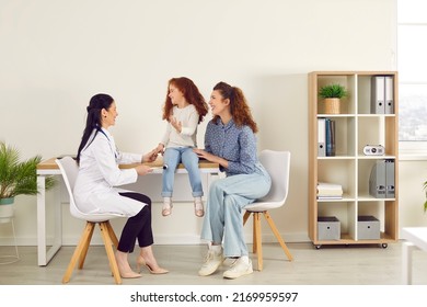 Friendly female doctor examining happy little patient in modern medical office interior. Cute cheerful preschool child and her mom laugh when professional neurologist uses hammer to test knee reflex