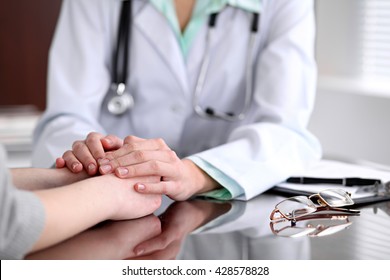 Friendly Female Doctor Hands Holding Patient Hand Sitting At The Desk For Encouragement, Empathy And Support While Medical Examination. Bad News Lessening, Compassion, Trust And Ethics Concept 