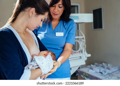 Friendly female doctor or nurse wearing blue scrubs uniform watching a new mother feed the baby with a breast in hospital ward. New born health, lactation concept. - Powered by Shutterstock