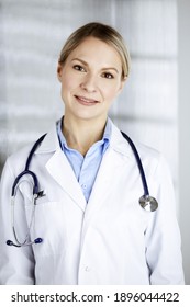 Friendly Female Doctor Standing In Clinic. Portrait Of Cheerful Smiling Physician. Perfect Medical Service In Hospital. Medicine And Healthcare Concept