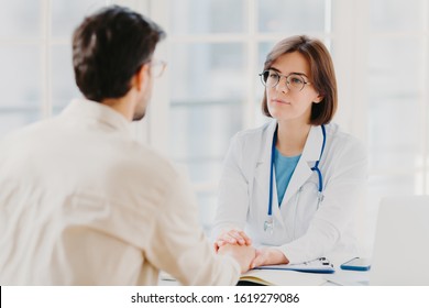 Friendly female doctor tries to support patient, holds his hands, gives useful consultation and explains medical information, makes diagnostic examining, pose in hospital room. Heathcare, assistance
