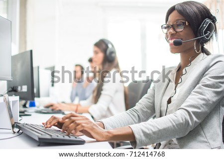 Friendly female helpline operator with headphones in office. Agent customer service representative: business and office concept.