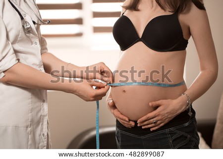 Friendly female medicine doctor holding centimeter tape and listening to pregnant woman standing for encouragement, empathy, cheering,support, medical examination. New life of abortion concept.
