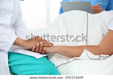 Friendly female medicine doctor's hands holding pregnant woman's hand lying in bed for encouragement, empathy, cheering and support while medical examination. New life of abortion concept