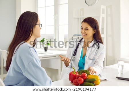 Friendly female nutritionist advises woman on diet plan and talk about benefits of raw vegetables. Doctor consults young female patient in hospital office. Concept of healthy eating and food science