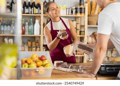 Friendly female salesperson offers to buy fresh cheese and dried meat to a male customer at a grocery store - Powered by Shutterstock