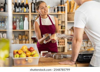 Friendly female salesperson offers to buy fresh cheese and dried meat to a male customer at a grocery store - Powered by Shutterstock