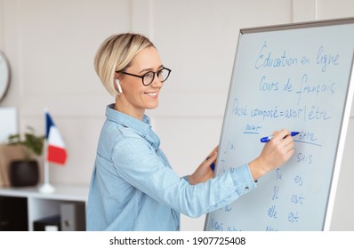 Friendly female teacher writing grammar rules on blackboard during online French lesson. Positive young tutor teaching foreign language on web. Remote education and tutoring concept