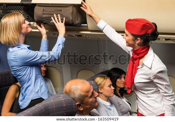 Friendly flight attendant helping passenger\
to put luggage cabin\
compartment
